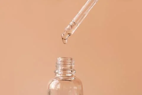 Opened cosmetic bottle with drop of face serum falling down from pipette Stock Photos