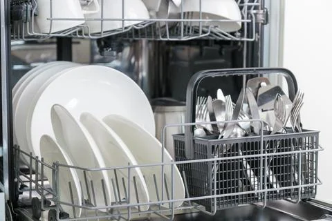 Opened dishwasher machine with clean tableware, white porcelain plates. Conve Foto stock