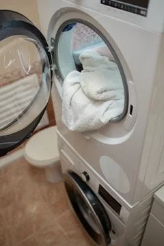 Opened dryer machine full of white clothes. Closeup. Front view. Stock Photos