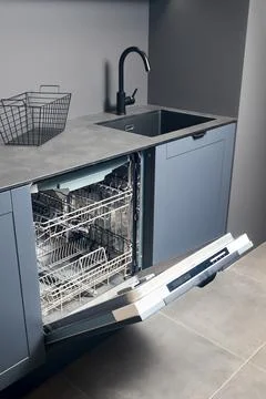 Opened empty dishwasher machine in contemporary blue grey kitchen with compact Stock Photos