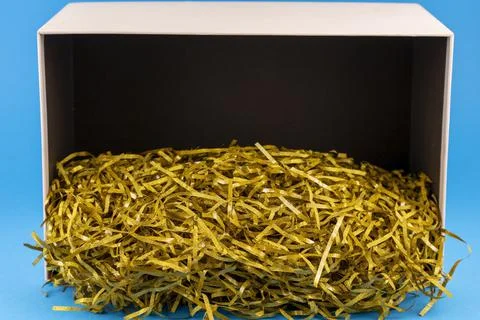 Opened gift box with decorative straw, filler, shavings. On a blue background 库存照片