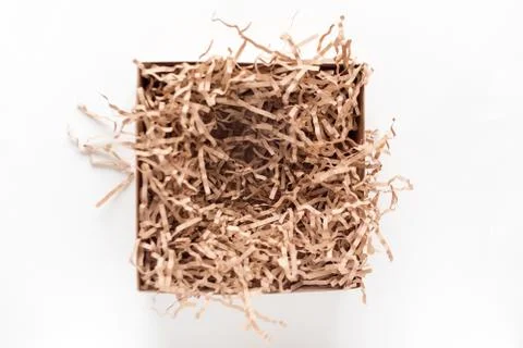 Opened gift box with decorative straws fillers on light background. Brown cra Stock Photos