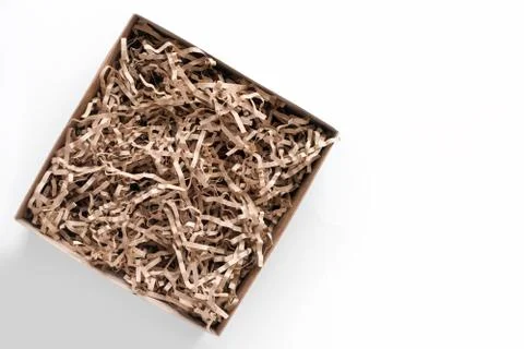 Opened gift box with decorative straws fillers on light background. Brown cra Stock Photos
