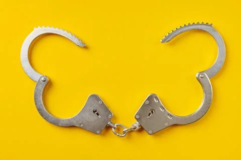 Opened handcuffs on yellow background. Stock Photos