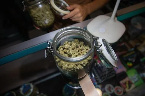 A opened jar filled with raw marijuana buds on a desk inside a coffee shop Stock Photos