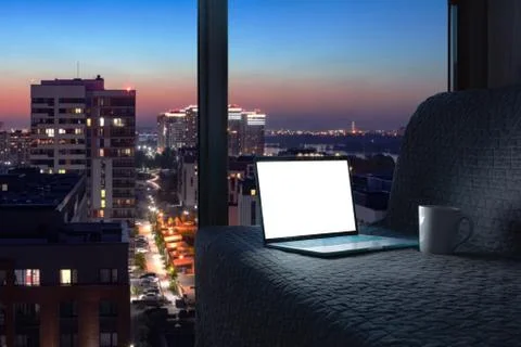 Opened laptop on grey sofa with panoramic view of night city from the window Stock Photos
