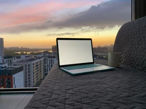 Opened laptop on grey sofa with panoramic view of night city from the window Stock Photos