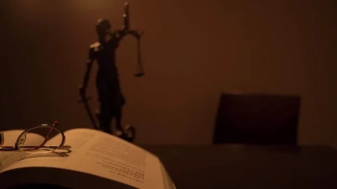 Opened Law Book on Judge's Table With Lady Justice Sculpture and Hummer Stock Footage 73833804
