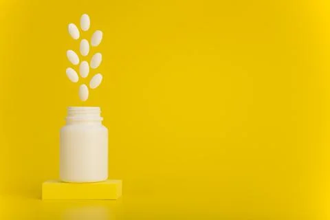 Opened medication bottle on podium with white oval pills jumping out against Stock Photos