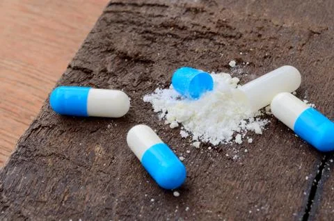 Opened medicine capsule pill with powder on wood background Stock Photos