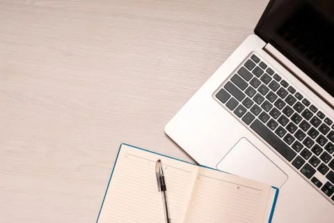 Opened notebook with black pen and silver laptop on a white wooden table, top Stock Photos