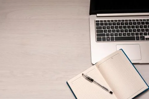 Opened notebook with black pen and silver laptop on a white wooden table, top Stock Photos