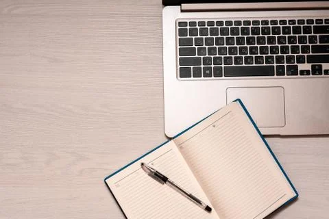 Opened notebook with black pen and silver laptop on a white wooden table, top Stock Photos
