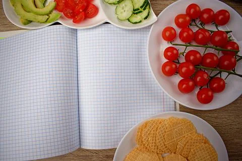 Opened notebook in a cage for notes. Around a snack of crackers and chopped Stock Photos