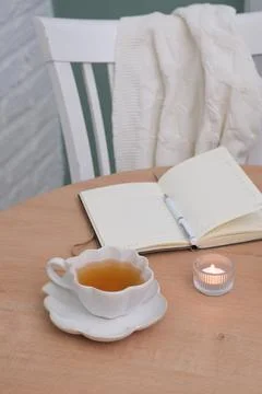 Opened notebook with white pen, a cup of tea and burning candle on wooden table Foto stock