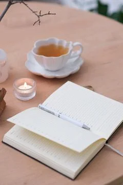 Opened notebook with white pen, a cup of tea and burning candle on wooden table Foto stock