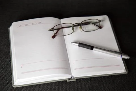 Opened notebook. Workplace with tablet, glasses and pen on a black background Stock Photos