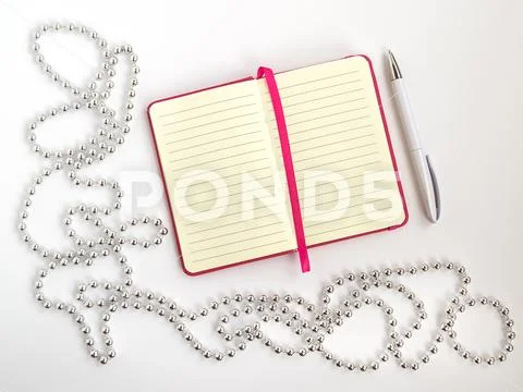 Opened notepad with lined paper, white ballpoint pen and silver bead ...