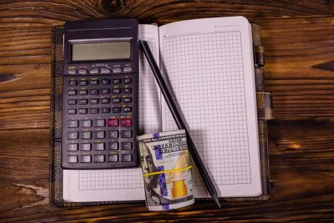Opened notepad, one hundred dollar banknotes, scientific calculator and penci Stock Photos
