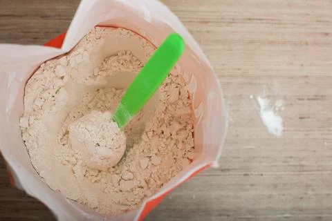 Opened package with flour and spoon inside on the kitchen table for cooking v Stock Photos