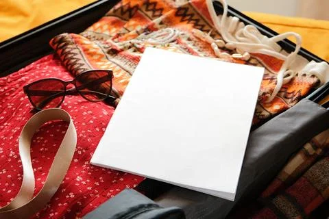 Opened packed suitcase on bed in hotel room with white magazine mockup Stock Photos