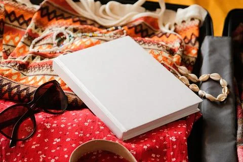 Opened packed suitcase on bed in hotel room with white book mockup Stock Photos