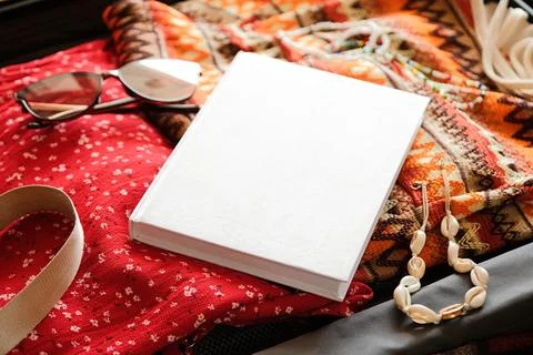 Opened packed suitcase on bed in hotel room with white book mockup Stock Photos