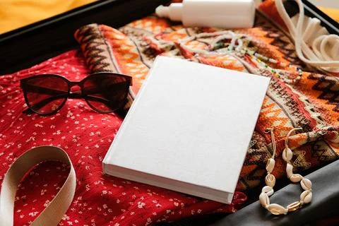 Opened packed suitcase on bed in hotel room with white book mockup Stock Photos