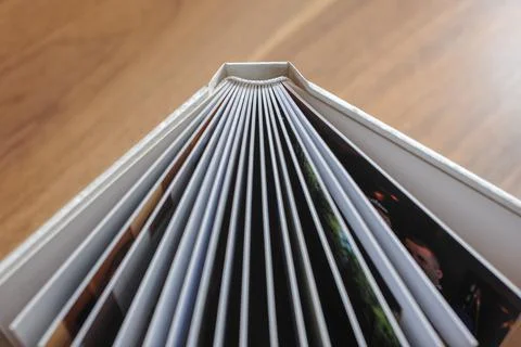 Opened photobook with thick plastic sheets in a hardcover on a wooden table b Stock Photos