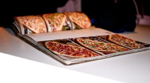 Opened pizza menu lying on white table Stock Photos