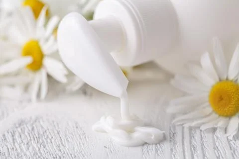 Opened plastic container with cream and chamomile flower on a light backgroun Stock Photos