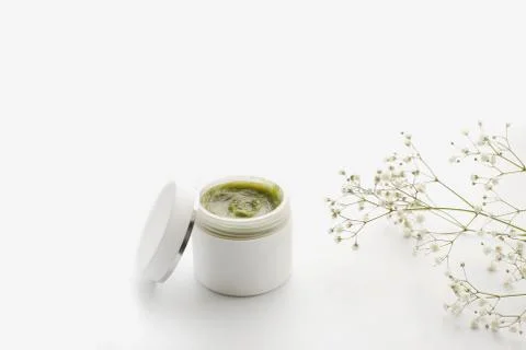 Opened plastic container with cream and flowers on a white background. face Stock Photos