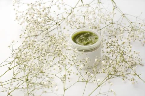 Opened plastic container with cream and flowers on a white background. face c Stock Photos