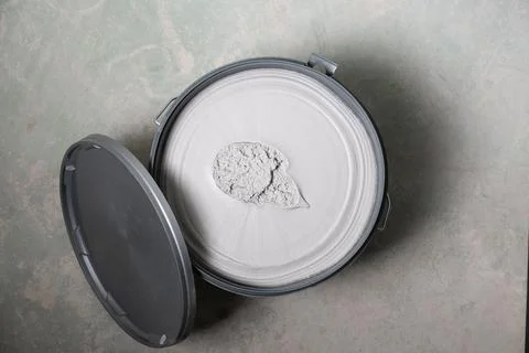 Opened plastic container with wall filler on concrete floor top view Stock Photos