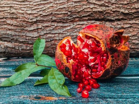 Opened pomegranate fruit with scattered ruby ​​seeds on a wooden table. Stock Photos