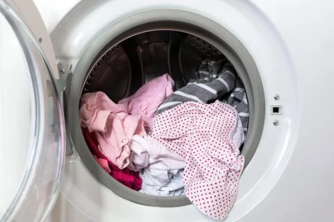 Opened round washing machine door with rotating garments inside. Focus in the Stock Photos