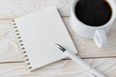 Opened spring notepad, white ballpoint pen and cup of coffee on a wood table Stock Photos