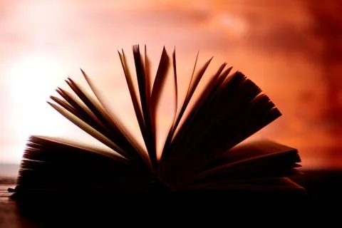 An opened thick book backlit by light on a brown background. Stock Photos
