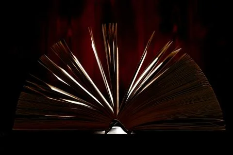 An opened thick book backlit by light on a brown background. Stock Photos