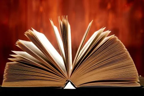 An opened thick book backlit by light on a brown background. Stock Photos