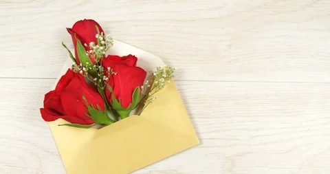 Opened yellow envelope with red roses on white wooden background 4k Stock Footage 99780513