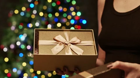 Opening Christmas present box in front of Christmas tree Stock Footage 143804956