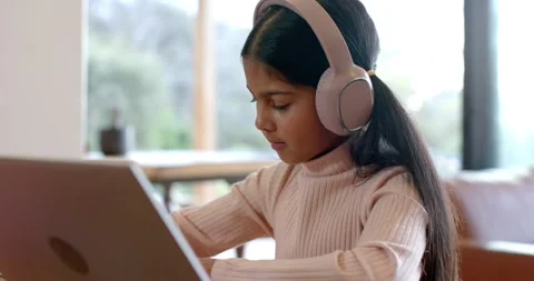 Opening laptop pulling on headphones, Indian girl writing notebook notes to Stock Footage 344219562