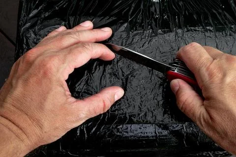 Opening a package wrapped in black stretch with a penknife, Stock Photos