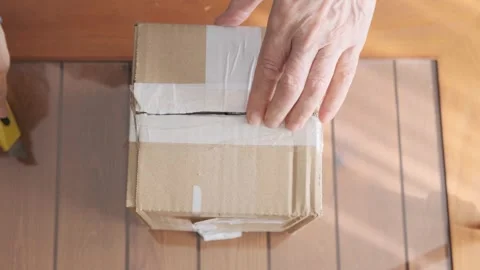 Opening a Sealed Cardboard Box Using a Yellow Utility Knife on Wooden Table. Stock Footage 309095466