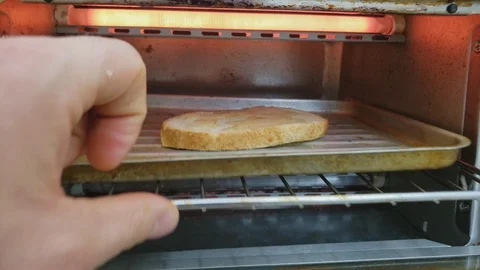 Opening small oven and checking slice of bread topped with butter being broiled 스톡 동영상 105537106