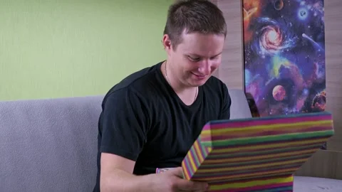 Opens the gift box. surprise and joy. a man in a dark T-shirt is sitting on the Stock Footage 168486326