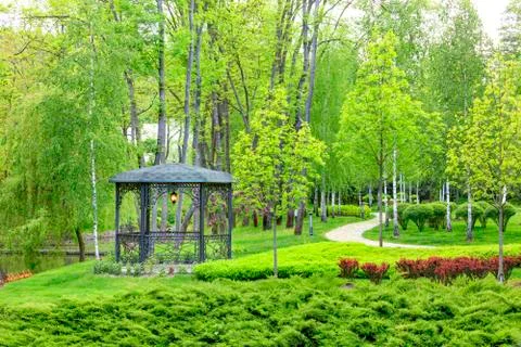 Openwork metal arbor with forged elements surrounded by beautiful spring park Stock Photos