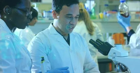 Operating male researcher using compound microscope at bench, wearing white lab Stock Photos