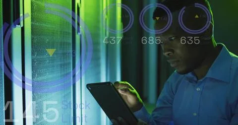 Operating mid-adult tech checking tablet in server rack aisle, wearing blue Stock Photos